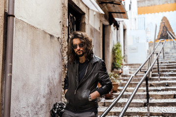 Fototapeta na wymiar Young bearded and long haired man wearing leather jacket and sunglases walking on the southern european street