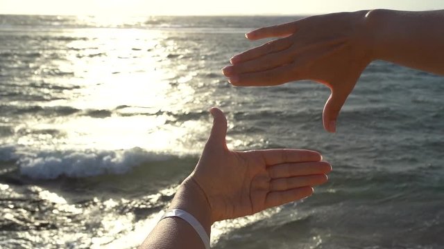 Point of view of beautiful two female hands making square with her hands isolated on sunrise sea water background. Woman standing at morning beach of hotel resort and enjoying magic marine landscape.