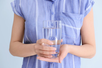Woman with glass of fresh water on light background, closeup