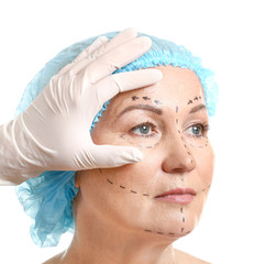 Plastic surgeon touching face of mature woman with applied marks on white background