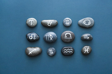 Stones with painted Zodiac signs on color background