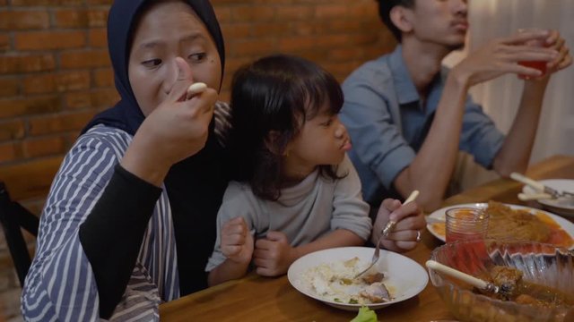 asian muslim mom eat with her daughter sitting on lap during dinner