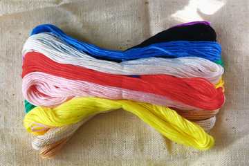 multi-colored colorful rainbow colors threads for embroidery floss on light fabric canvas close-up,...