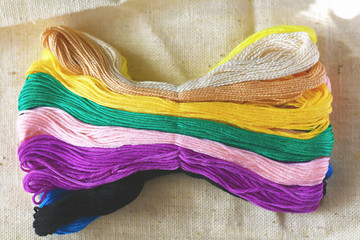 multi-colored colorful rainbow colors threads for embroidery floss on light fabric canvas close-up,...