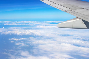 Obraz premium Airplane flying on blue sky and white cloud. Wing of an airplane flying above the cloud looks from the window of the plane. 