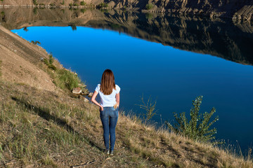 Naklejka premium horizontal photo with a beautiful young girl standing on top of a cliff above a clear blue lake on a sunny summer day during a hike
