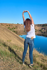 young beautiful girl doing exercises and stretching on a rock overlooking a clear blue lake on a clear sunny day