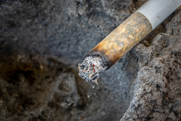 A smoldering Cigarette with ash on the edge of an ashtray made of solidified lava. Close up. Copy...