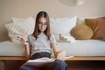 Cute teenager girl sitting on the floor at home with books and doing homework. Education, children and school concept, distance learning, self education    