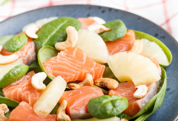 Fresh salmon with pineapple, spinach and cashew in blue ceramic plate on a gray concrete background.
