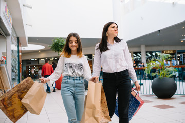 Beautiful young mom and teenage daughter are holding shopping bags and smiling while doing shopping in mall. Family shopping.
