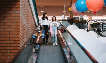 Beautiful young mom and teenage daughter are holding shopping bags and smiling while doing shopping in mall. Family shopping.