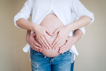 Pregnant woman with her husband hugging tummy, heart symbol on belly. Concept of Pregnancy health care      