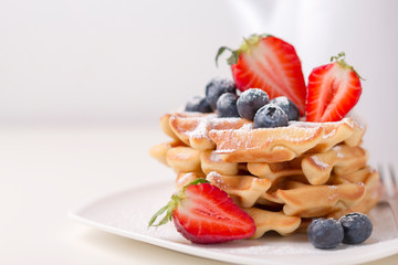 Stack of delicious .vanilla flavor waffles with blueberries and sliced strawberries .close-up on white background, copy space.