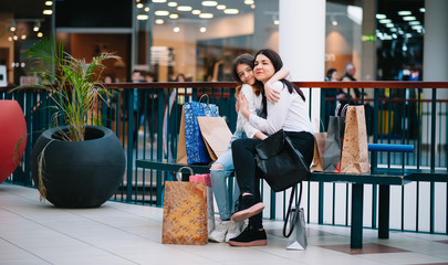 Beautiful young mom and teenage daughter are holding shopping bags and smiling while doing shopping in mall. Family shopping.