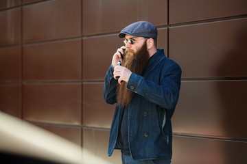 Vape bearded man. An adult man with a very long beard in a cap and sunglasses smokes an electronic...