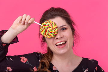 Fashion, glamour and people concept - young funny woman closed her eye with lollipop on pink background