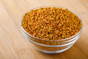 Fenugreek seeds in glass bowl and scoop on wooden background