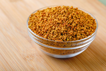 Fenugreek seeds in glass bowl and scoop on wooden background