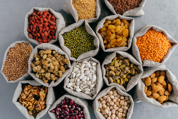 Dried food, harvest and protein from plant concept. Set of small hessian sacks filled with legumes, buckwheat, walnuts, banyan, chickpeas, muleberry and other.