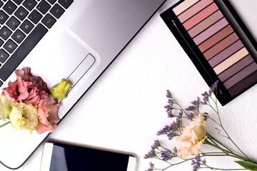 Laptop with flowers and cosmetics on white table. Freelancer workspace.