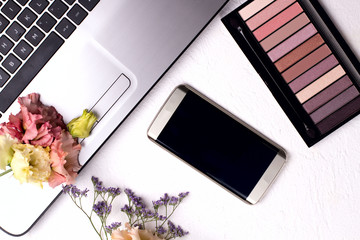 Laptop with flowers and cosmetics on white table. Freelancer workspace.