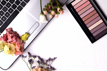 Laptop with flowers and cosmetics on white table. Freelancer workspace.