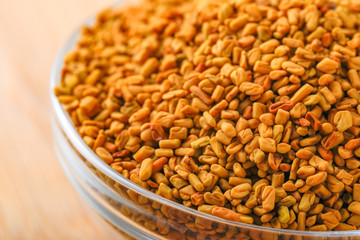 Fenugreek seeds in glass bowl and scoop on wooden background