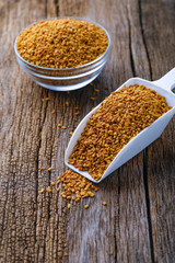 Fenugreek seeds in glass bowl and scoop on wooden background
