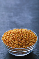 Fenugreek seeds in glass bowl and scoop on wooden background
