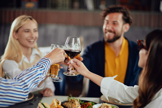 Four Happy Muliethnic Freinds Dressed Smart Casual Cheering With Alcohol While Sitting At Restaurant.