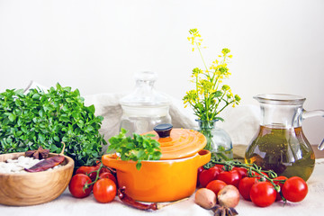 Food and utensils to prepare food. Fresh basil, cherry tomatoes, beans, olive oil, lime, onion, spices, saucepan, jars in cereals. Culinary background. Copy space