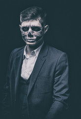 Stylish and beautiful, emotional young man with skeleton makeup in a strict suit against the background of smoke and dark background to Halloween