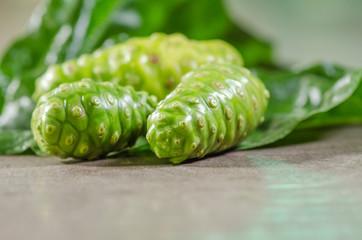 Fruit of Great morinda (Noni) or Morinda citrifolia tree and green leaf on the wood background