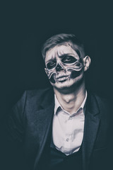 Stylish and beautiful, emotional young man with skeleton makeup in a strict suit against the background of smoke and dark background to Halloween