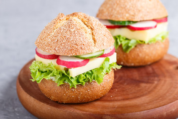 sandwiches with cheese, radish, lettuce and cucumber on wooden board on a gray concrete background.