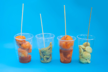 A various Filipino street foods on a plastic cup with sticks on blue isolated background. Philippines street foods and their names such as Kwek - Kwek, Fishball, and Kikiam.
