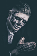 Stylish and beautiful, emotional young man with skeleton makeup in a strict suit against the background of smoke and dark background to Halloween