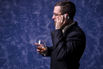 Business man with a glass of brandy and a smartphone.