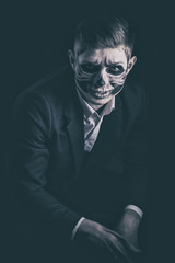 Stylish and beautiful, emotional young man with skeleton makeup in a strict suit against the background of smoke and dark background to Halloween