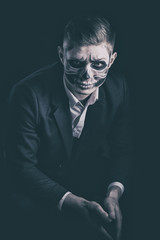 Stylish and beautiful, emotional young man with skeleton makeup in a strict suit against the background of smoke and dark background to Halloween