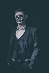 Stylish and beautiful, emotional young man with skeleton makeup in a strict suit against the background of smoke and dark background to Halloween
