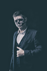 Stylish and beautiful, emotional young man with skeleton makeup in a strict suit against the background of smoke and dark background to Halloween