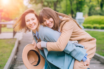 Two adult playfull good looking women sisters in trendy coat piggybacking her pretty girlfriend in...