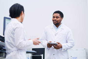 Content multi-ethnic medical colleagues in white coats standing in laboratory and discussing scientific project