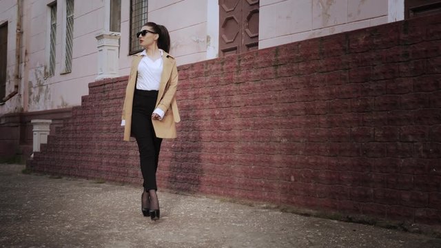 trendy lady with gorgeous makeup in classic clothes walks past terracotta wall low angle shot slow motion