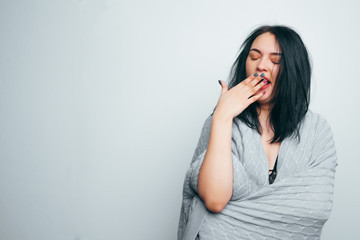 A beautiful brunette girl in a gray plaid is yawning covering her hands. Drowsiness, stress, desire to relax and rest. Gray studio background.