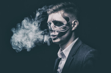 Stylish and beautiful, emotional young man with skeleton makeup in a strict suit against the background of smoke and dark background to Halloween