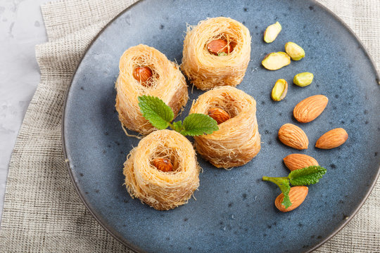 Kunafa, traditional arabic sweets in blue ceramic plate on a gray concrete background.