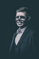 Stylish and beautiful, emotional young man with skeleton makeup in a strict suit against the background of smoke and dark background to Halloween